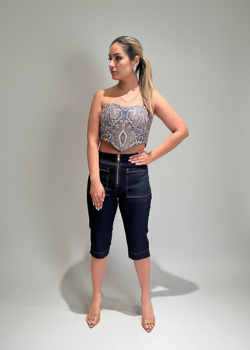 Woman wearing a patterned top and dark jeans against a plain background