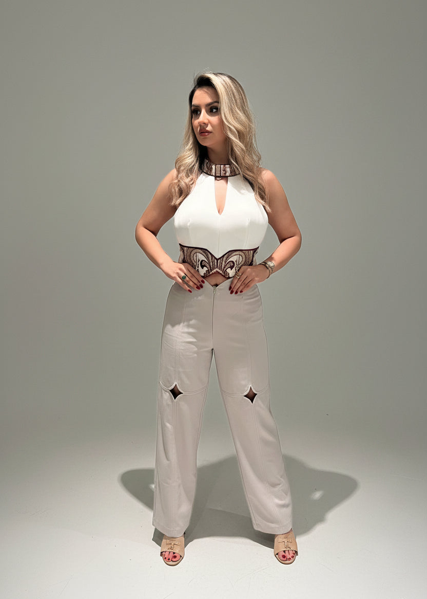 Woman wearing a white top with a butterfly design and beige pants on a gray background