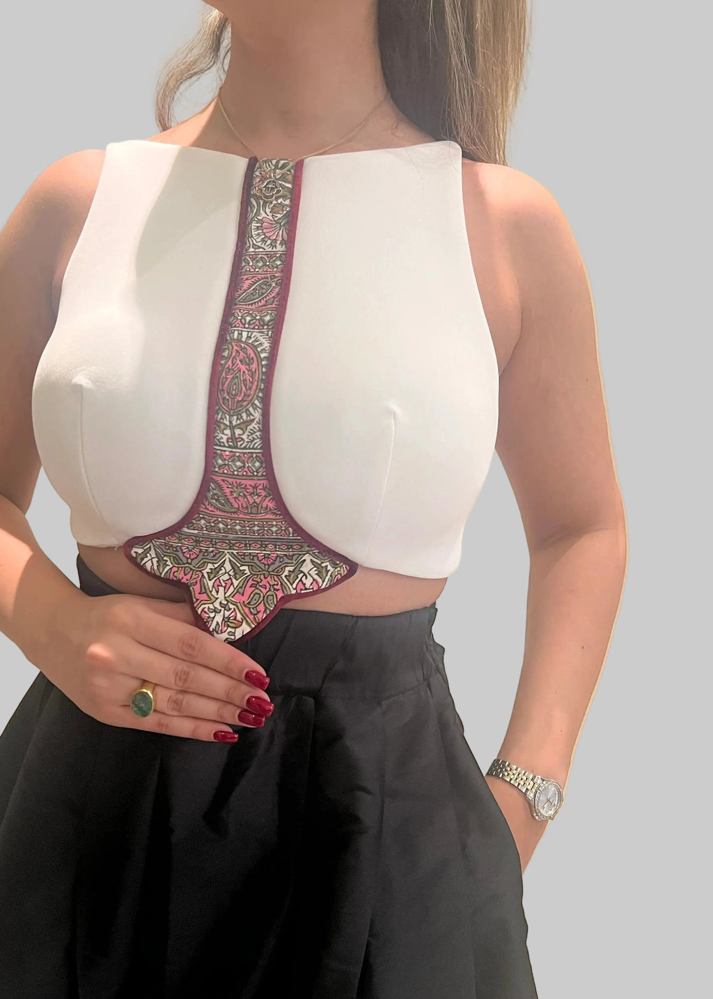 White sleeveless top with intricate embroidery on a strap, worn by a person against a neutral background.