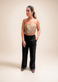 Woman wearing a gold strapless top and black pants against a gray background