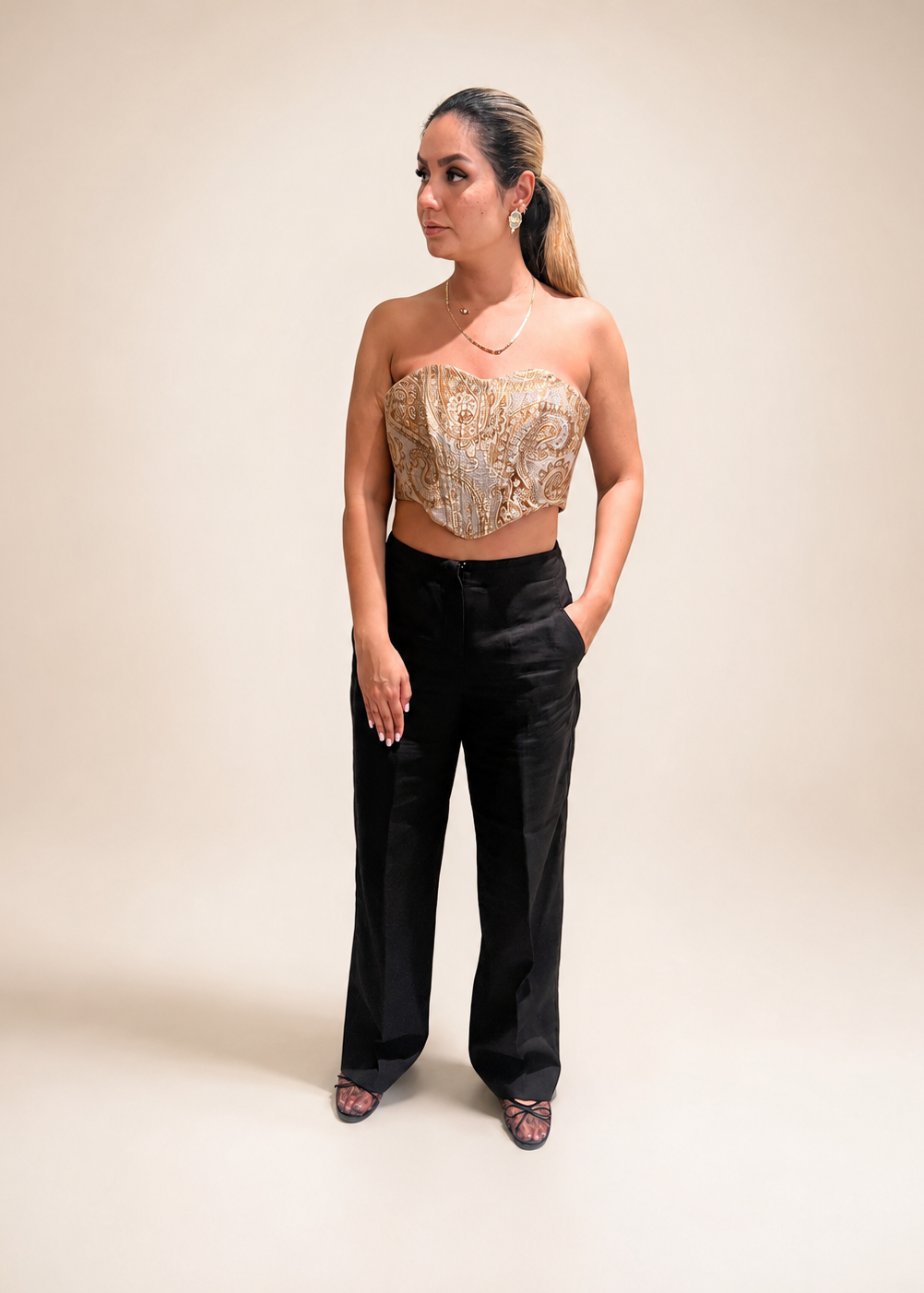 Woman wearing a gold strapless top and black pants against a gray background